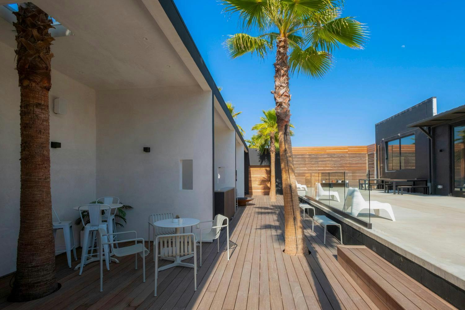 A chic and tranquil outdoor patio with wooden decking, palm trees, and minimalist furniture, perfect for relaxation.