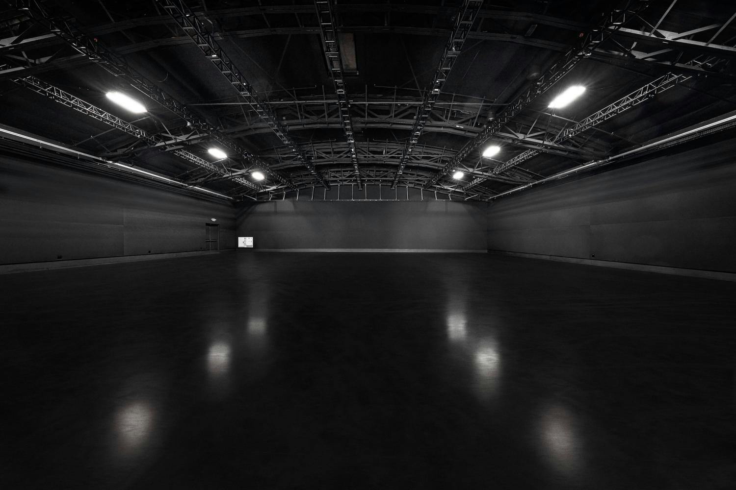 A dark, empty industrial studio with overhead stage lighting and polished floors.
