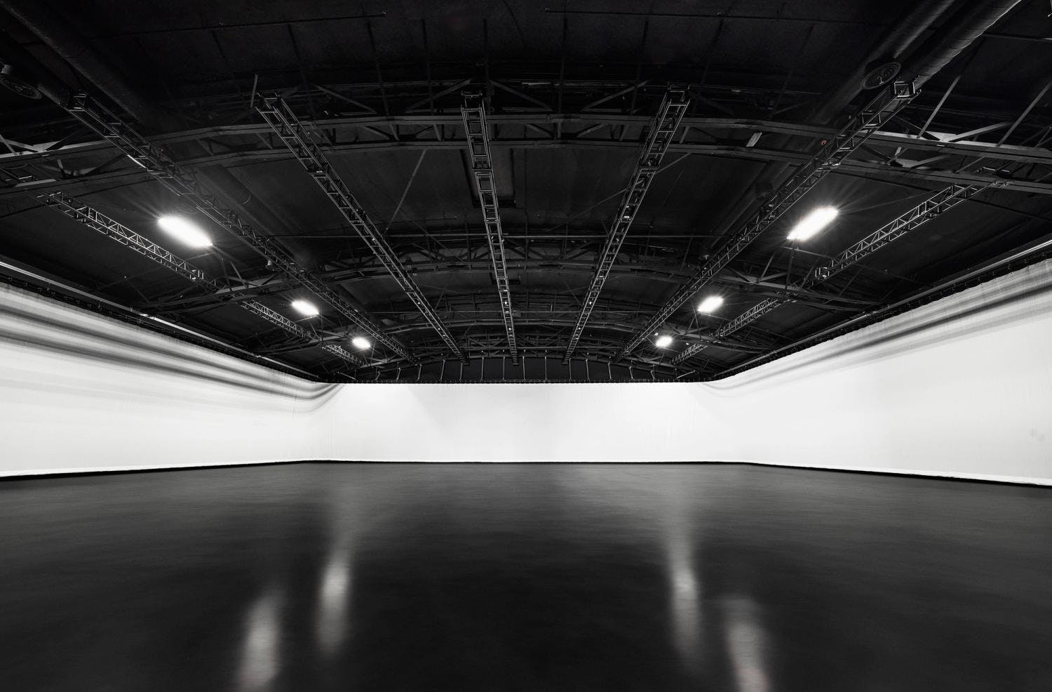 A spacious indoor studio with a curved white cyclorama wall and ceiling rigging for stage lighting.