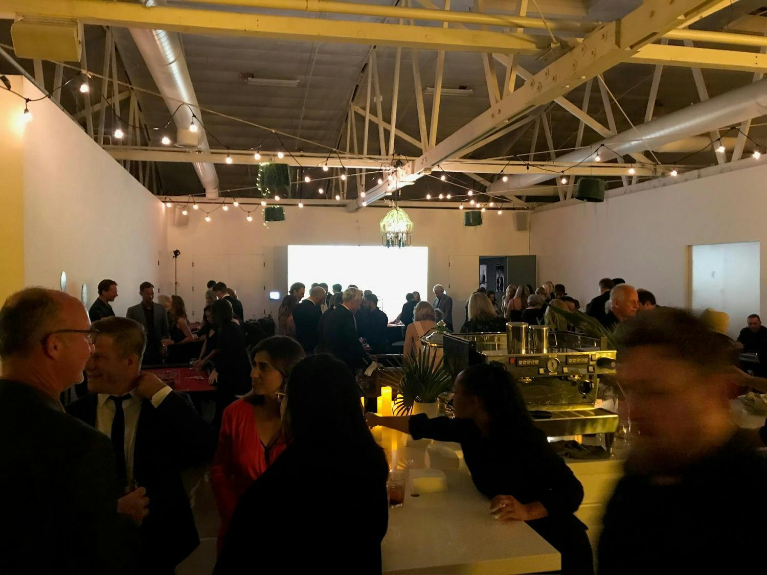 A gallery soirée with people engaged in conversation, accented by warm lighting and the gallery's structural white beams.