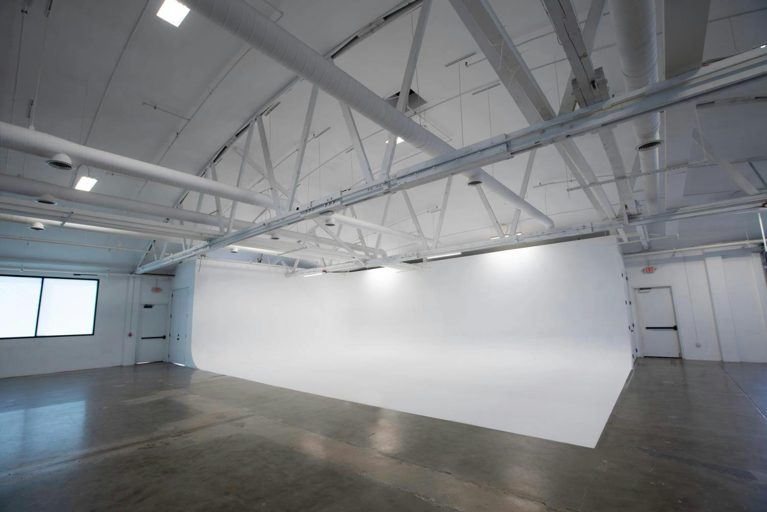 An expansive white cyclorama wall within a spacious studio with industrial white ceilings and ductwork, designed for professional photography and video productions.