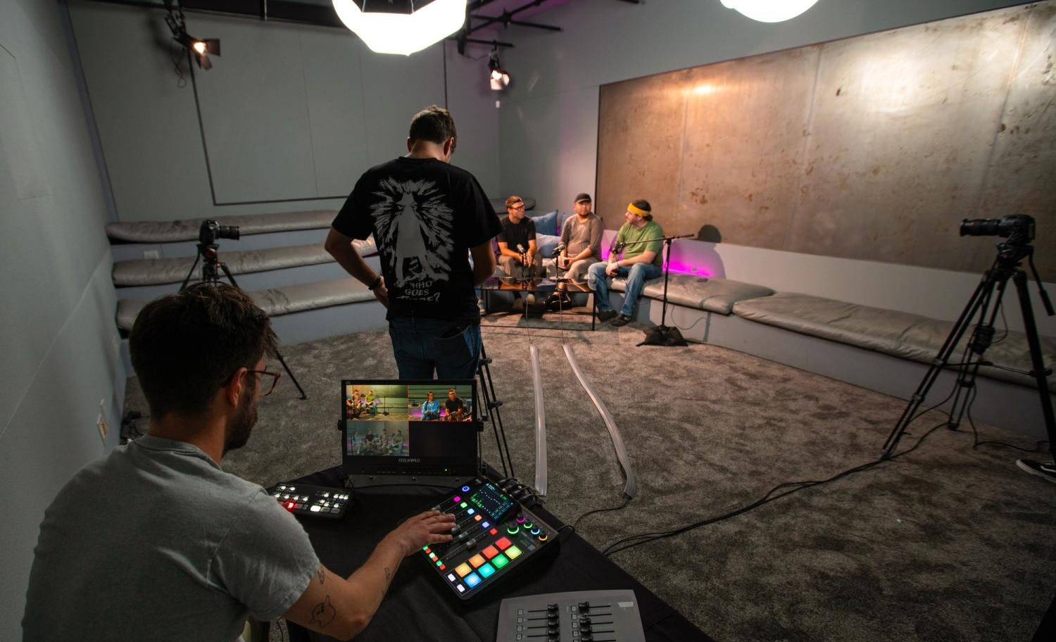 A behind-the-scenes view of a video recording set-up, focusing on the camera's display screen showing two people being filmed.