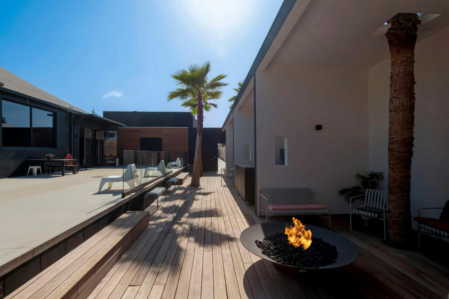 An elegant outdoor space featuring a fire pit, comfortable seating, and wooden decking, under a bright blue sky.