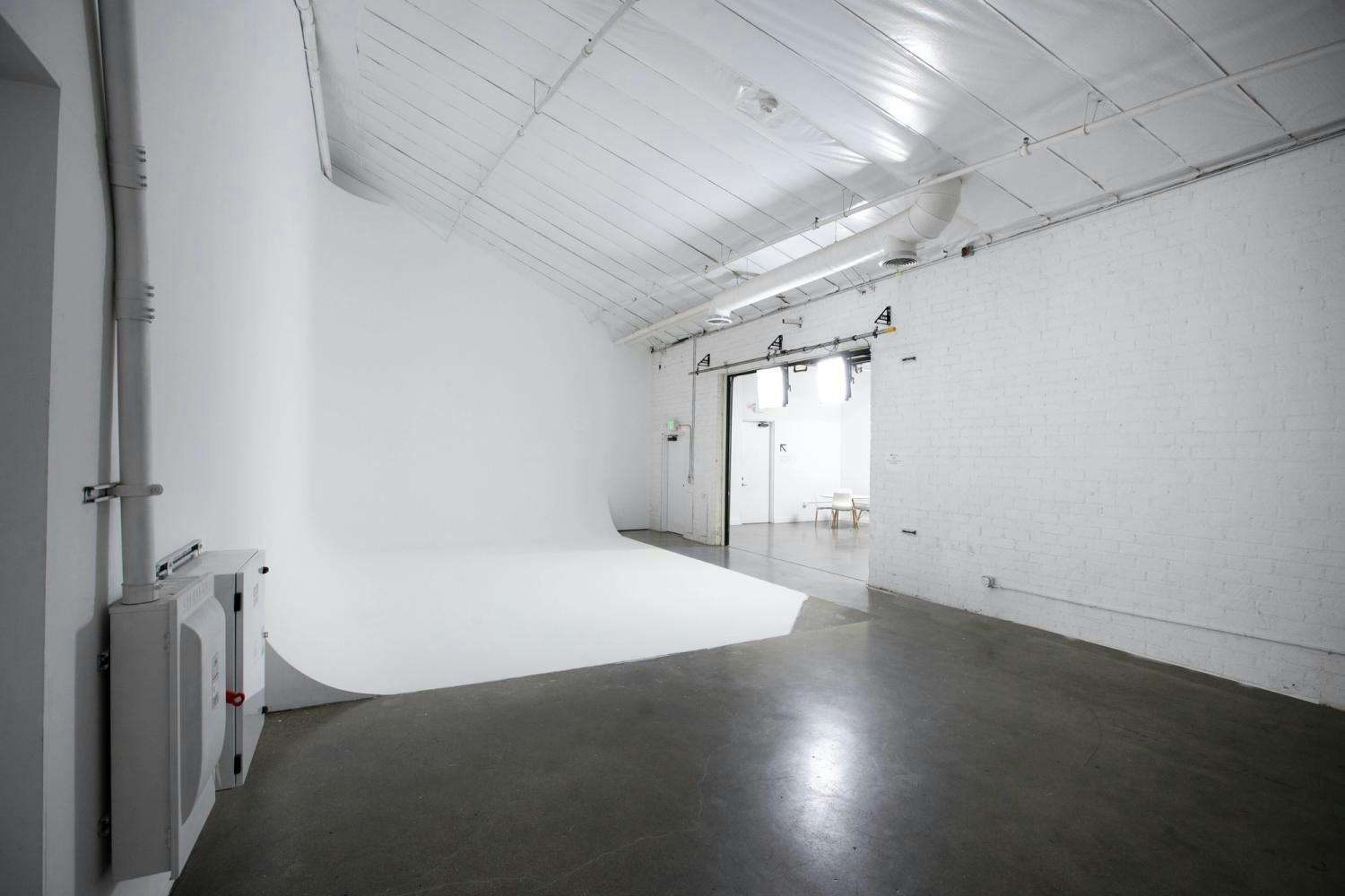  A modern photo studio with a white cyclorama, glossy concrete flooring, and white brick walls under a white industrial ceiling.