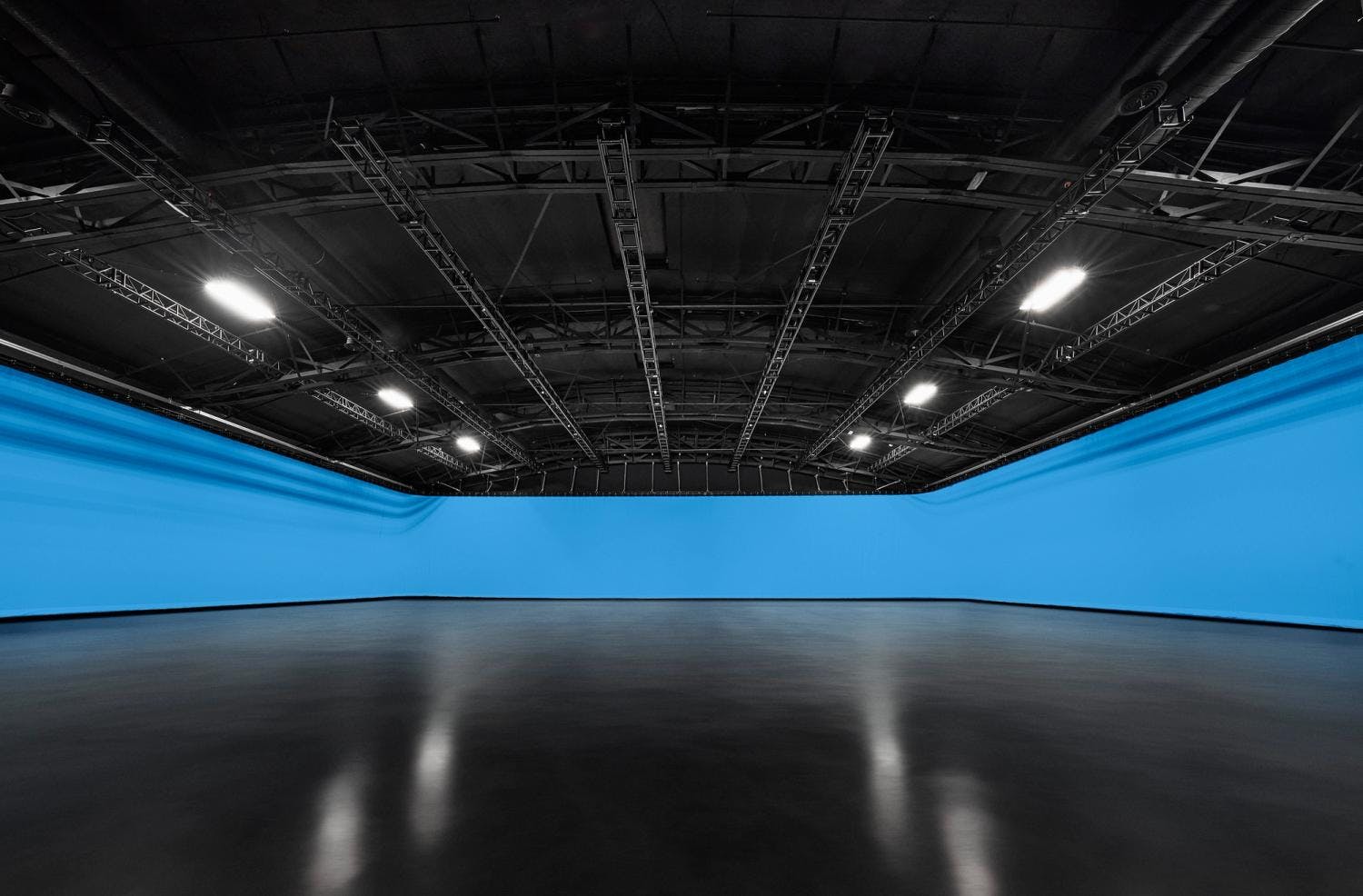 A spacious indoor studio with a curved blue cyclorama wall and ceiling rigging for stage lighting.