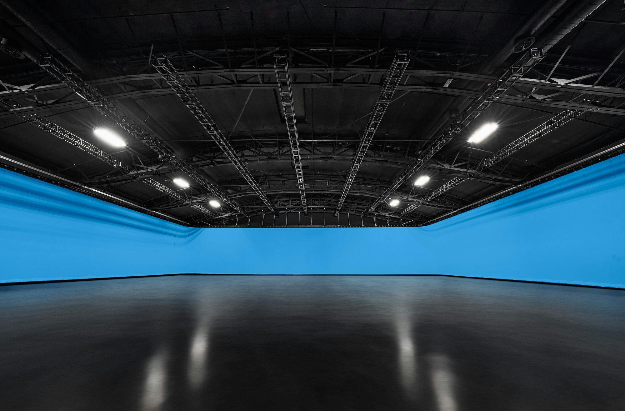 An expansive studio with a glossy black floor and curved blue cyclorama under a grid of ceiling-mounted studio lights.