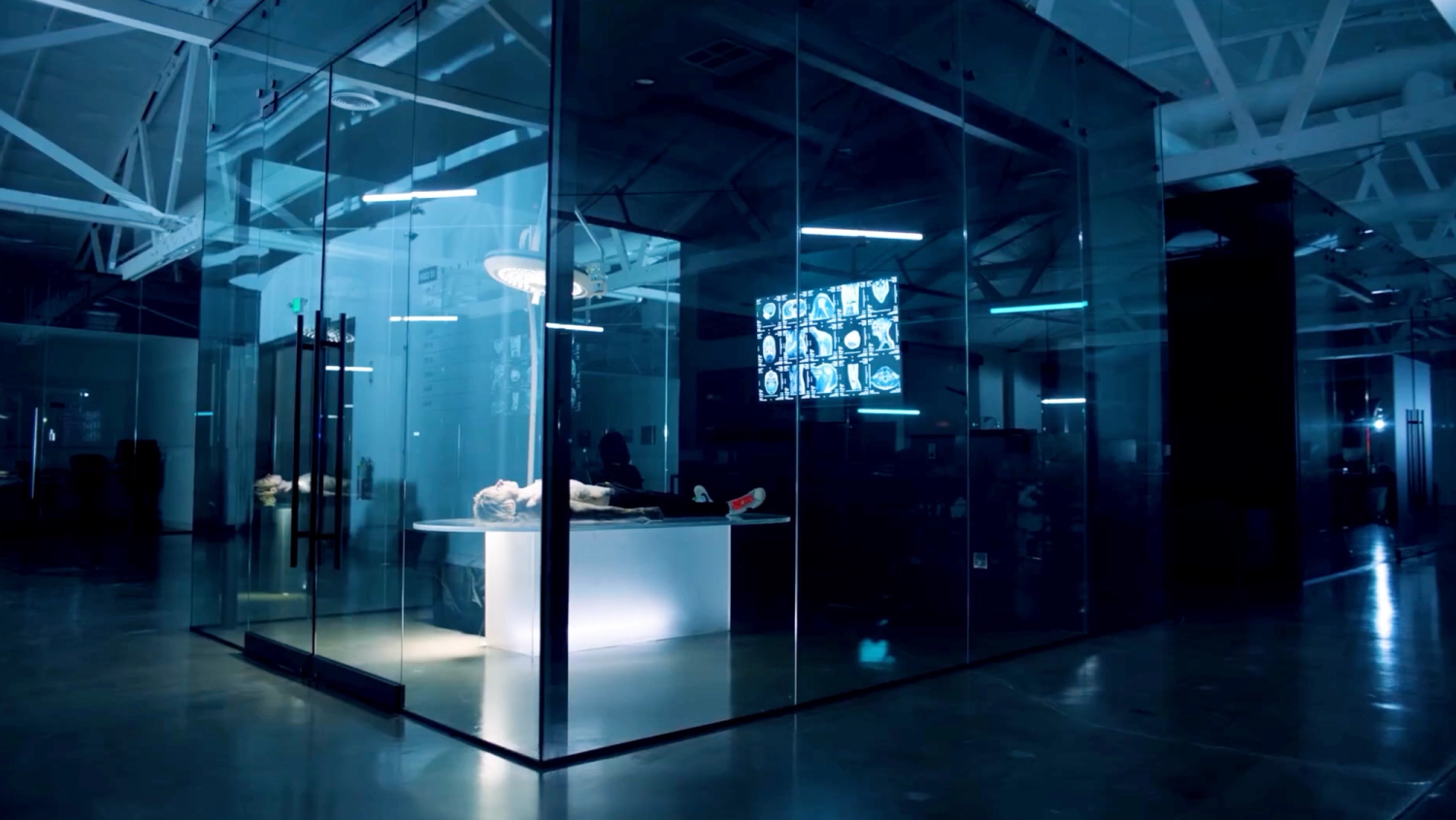 A cube space used as futuristic medical room with a person lying on a table and X-ray images displayed on screens in a dark, blue-lit environment.