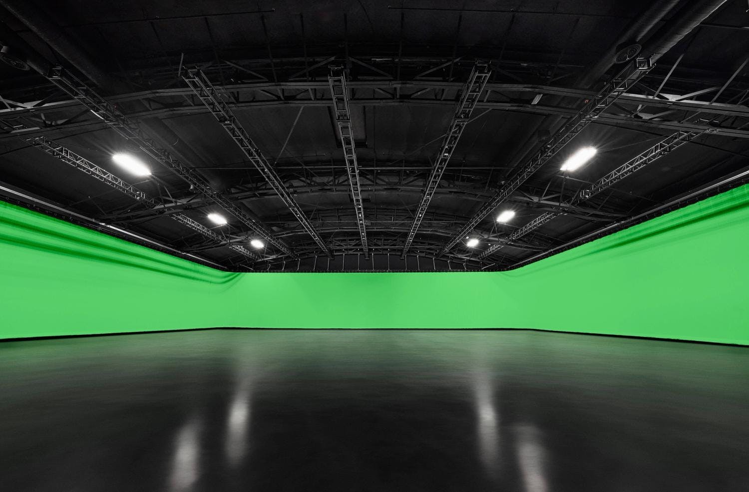 A spacious indoor studio with a curved green cyclorama wall and ceiling rigging for stage lighting.