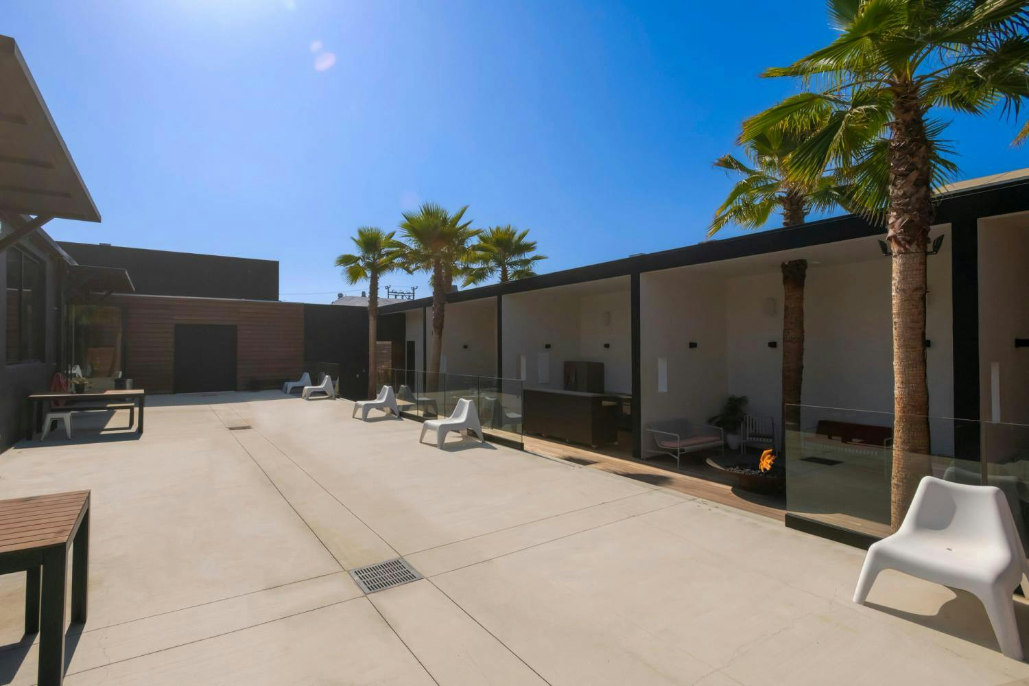 A modern outdoor patio area with stylish seating, surrounded by sleek architectural elements and palm trees.