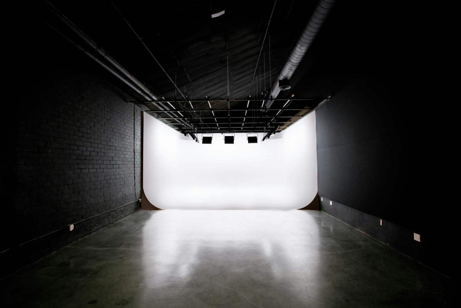 A professional photo studio with a white cyclorama and a grid of ceiling-mounted lights casting a soft glow on the curved backdrop.