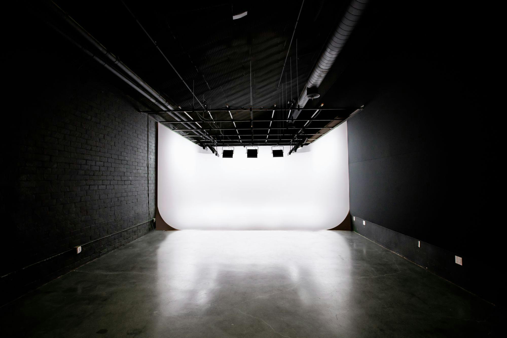 The image shows Studio B with a spacious, well-lit three-walled cyclorama and an 11-foot grid overhead, surrounded by dark walls and a polished concrete floor.