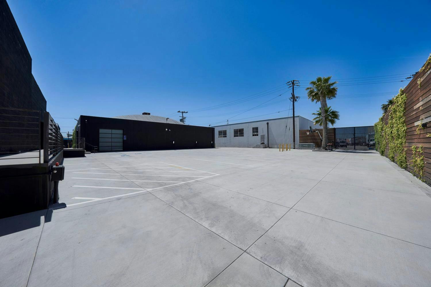 Perspective of a large black warehouse building with minimalistic design, featuring a clear and empty concrete parking lot.